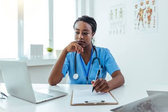 Nurse practitioner at a desk beside an anatomy chart