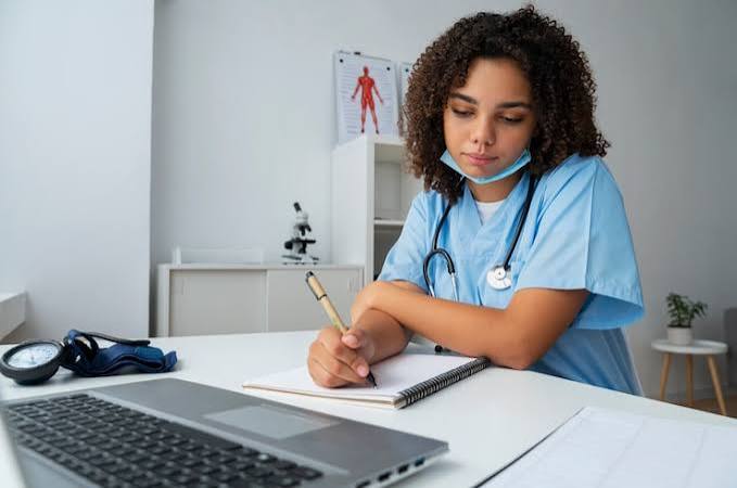 Nursing student writing notes at a clinic desk